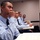 Four young individuals in matching light blue uniform shirts with dark neckties are seated in a row in a classroom setting. The person in the foreground, whose name tag reads 'BAMBA', rests their chin on their fist in a contemplative pose while looking forward. Open notebooks and documents are visible on their desks, suggesting an active instructional session.