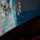 CBP Support to Super Bowl LIV A computer monitor displays a maritime tracking or navigation software interface showing a coastal city with a port area and numerous vessel icons clustered offshore. The display appears to show AIS (Automatic Identification System) or similar ship-tracking data with a radar sweep overlay emanating from a fixed point near the harbor. A gaming keyboard with RGB lighting is partially visible at the bottom of the frame.