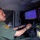CBP Support to Super Bowl LIV A U.S. Customs and Border Protection (CBP) Border Patrol agent is seated inside a mobile surveillance or command vehicle, operating a workstation with multiple monitors. The screens display what appears to be thermal/infrared camera footage showing a vehicle in a desert or open terrain environment. The agent is actively working at a keyboard while monitoring the surveillance feeds.