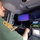 CBP Support to Super Bowl LIV A uniformed officer, identifiable by a shoulder patch consistent with U.S. Customs and Border Protection (CBP), is operating surveillance equipment inside what appears to be a mobile command or surveillance vehicle. The operator is using a FLIR-branded control console with a joystick while monitoring multiple screens displaying thermal and standard camera feeds. The setup suggests a remote surveillance or drone/camera operation in a field environment.