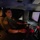 CBP Support to Super Bowl LIV A U.S. Customs and Border Protection (CBP) officer is seated inside a surveillance vehicle at night, operating what appears to be a FLIR (Forward Looking Infrared) camera system. The officer is working at a console with multiple monitors and control equipment, suggesting active surveillance or monitoring operations. The interior is dimly lit with red ambient lighting from the equipment.
