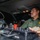 CBP Support to Super Bowl LIV A uniformed officer, identifiable by a green shirt with a shoulder patch consistent with U.S. Border Patrol, is seated inside a vehicle equipped with specialized law enforcement equipment. He is operating or monitoring a control panel with knobs, switches, and a prominent red toggle, while looking toward the windshield. A Motorola radio unit is visible mounted to the left side of the interior.