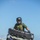 CBP Support to Super Bowl LIV A U.S. Border Patrol Federal Agent is riding a Can-Am Outlander ATV on a sandy beach with turquoise water visible in the background. The agent is wearing full protective gear including a helmet, tactical vest, and gloves. The ATV is olive/sage green and equipped with a front storage box and emergency lights.