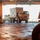 AGILE DEFENDER 2020 A tan/desert-colored military truck, consistent with a FMTV (Family of Medium Tactical Vehicles), is being loaded or unloaded from what appears to be a military roll-on/roll-off (RoRo) cargo vessel. The truck is hauling a white military container on a flatbed trailer through the ship's vehicle bay opening. The interior deck is wet and reflective, with a red vehicle or equipment partially visible in the foreground.