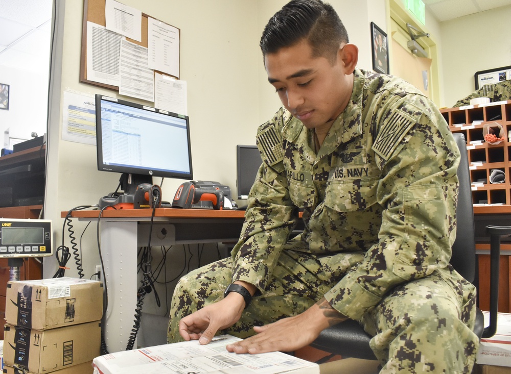 Logistics Specialist Seaman Keith Amarillo places barcodes on packages at the post office