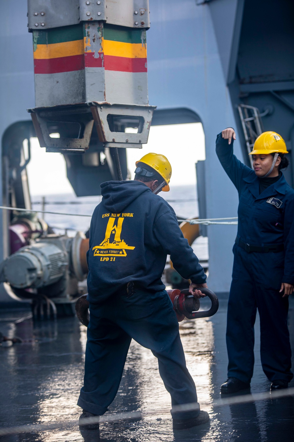 Sailor directs crane operato while Sailor waits to attach a insulated hook