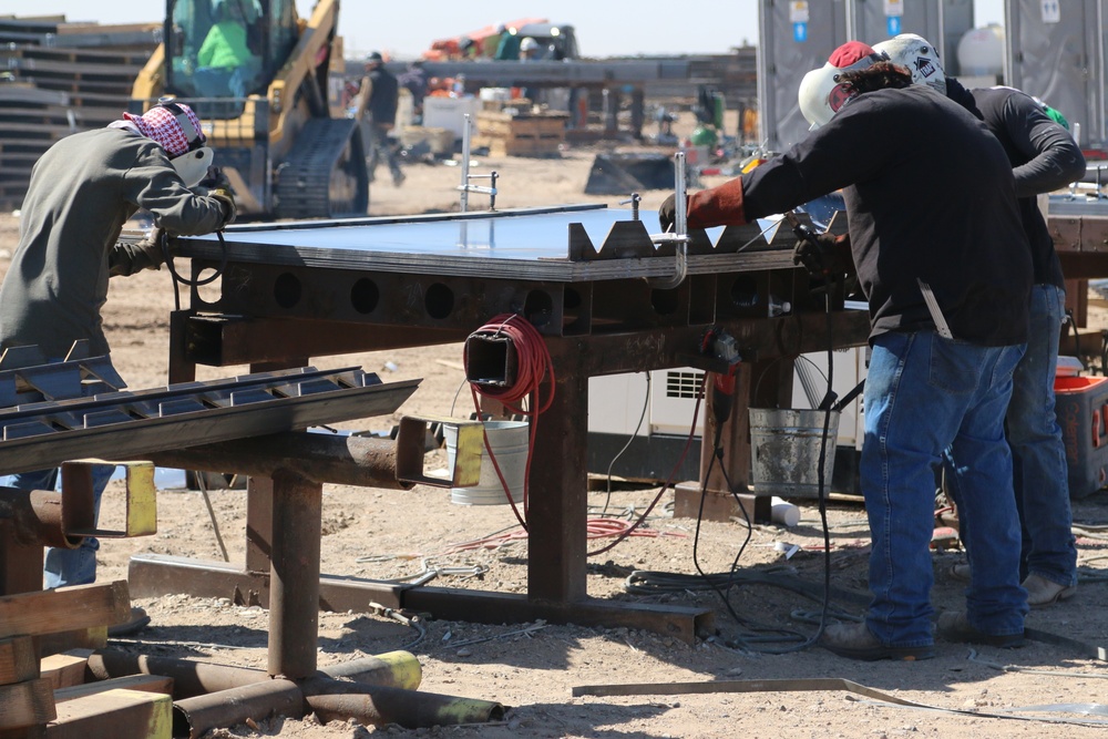 Workers weld brackets on the anti-climb plates during construction of the border barrier panels