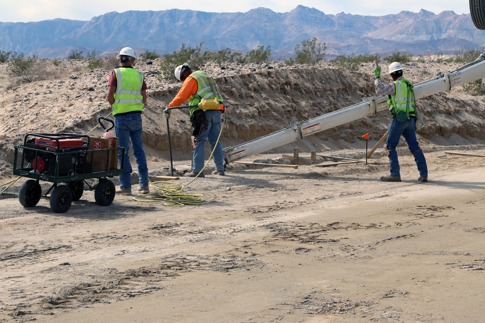 Crews place concrete into a trench that will secure a 30-foot bollard barrier panel at Heading Two at the El Centro 1