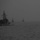 Three naval vessels are navigating in formation through heavily foggy, low-visibility conditions at sea. The foreground vessel is clearly identifiable as a US Navy warship, flying an American flag from its mast structure. Two additional vessels are visible in the background, partially obscured by dense fog or haze.