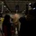 A military service member in camouflage uniform is being interviewed by television news crews inside what appears to be a large warehouse or food bank facility. Two camera operators flank the scene while a reporter holds a microphone toward the subject. Additional military personnel can be seen working in the background of the warehouse.
