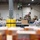 Military personnel in camouflage uniforms are volunteering at what appears to be a food bank or distribution warehouse. Multiple soldiers are packing and organizing boxes and food items along assembly-style tables. A green 'Fresh Produce' banner is visible in the background, confirming this is a food distribution facility.