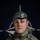 NATO BG-P EIB and ESB awardees A British Army soldier named McGrath is photographed in a formal portrait against a NATO flag backdrop. The soldier is wearing MultiTerrain Pattern (MTP) camouflage uniform with a grey beret bearing a regimental badge, along with NATO eFP Battle Group patches. The image appears to be an official NATO Enhanced Forward Presence (eFP) Battle Group Poland promotional photograph.