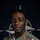 NATO BG-P Soldiers test on EIB and ESB tasks A U.S. Army soldier named Olowoshile is photographed in a formal portrait setting against a NATO flag backdrop. The soldier is wearing the Army Combat Uniform (ACU) in MultiCam pattern with visible U.S. Army and NATO-OTAN eFP Battle Group patches. The image appears to be an official NATO Enhanced Forward Presence (eFP) promotional portrait.