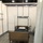 The image shows a temporary medical facility station set up inside a large convention center or warehouse space. A single hospital bed with side rails and casters is positioned within a modular partition cubicle, equipped with basic medical infrastructure. The setup appears to be part of a field hospital or emergency overflow medical facility.