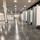 A large indoor facility, likely a convention center or arena, has been converted into a temporary medical or field hospital setup. Rows of individual cubicles are separated by gray privacy curtains hung on metal rails along the right side, with white partition walls visible on the left. The space appears to be in a ready or partially operational state with no patients or staff currently visible.