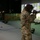 Two military personnel in different camouflage uniforms are participating in a firearms simulation training exercise. They are aiming simulated rifles at a large projected screen displaying a forested outdoor environment. The setting appears to be an indoor virtual marksmanship training facility.