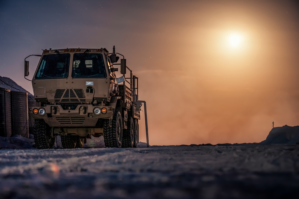 An armored FMTV is parked under a full moon at Al Asad Air Base, Iraq