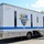 A large white mobile dental unit truck belonging to the Naval Dental Clinic Norfolk, designated MDU 10 (Mobile Dental Unit Number 10). The vehicle features a prominent shield-shaped logo with a caduceus symbol, a blue horizontal stripe, and patriotic imagery including a bald eagle and American flag on the rear. The motto 'Fit to Bite, Fit to Fight' is visible on the lower rear section of the unit.