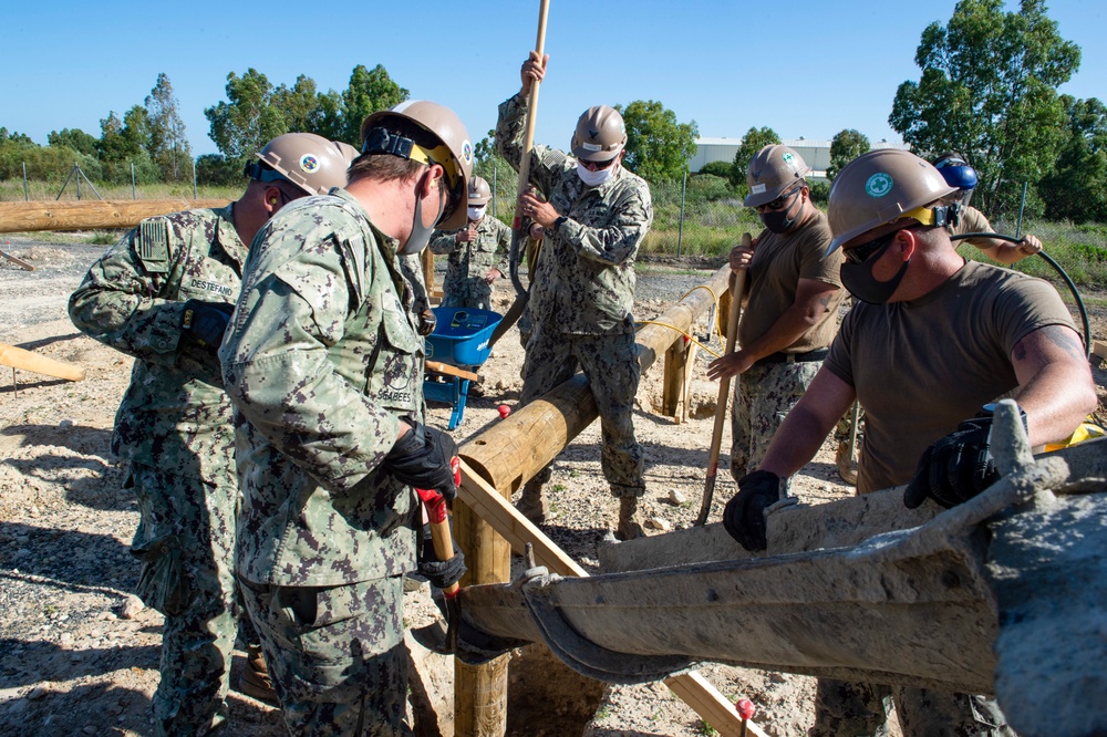 NMCB 1 Seabees fill post holes with concrete during an obstacle course construction project.