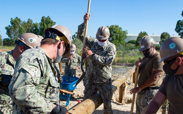 NMCB 1 Seabees fill post holes with concrete during an obstacle course construction project.