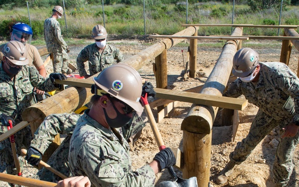 NMCB 1 Seabees fill post holes with concrete during an obstacle course construction project.