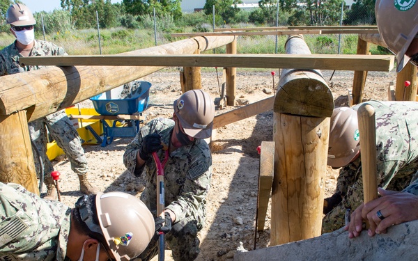 NMCB 1 Seabees fill post holes with concrete during an obstacle course construction project.