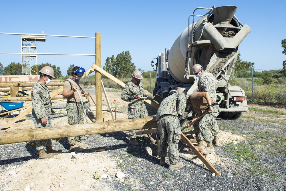 NMCB 1 Seabees fill post holes with concrete during an obstacle course construction project.