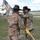 1st Battalion, 8th Cavalry Regiment Change of Command Two U.S. Army soldiers in OCP (Operational Camouflage Pattern) uniforms and black cavalry Stetson hats are participating in a military ceremony, likely a change of command or activation ceremony. One soldier is passing or receiving a unit guidon (flag) with colorful streamers attached, representing campaign and unit honors. The ceremony is taking place on a military installation parade field with other soldiers and buildings visible in the background.