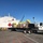 A white flatbed semi-truck loaded with palletized cargo wrapped in yellow coverings is positioned at a port dock alongside the USNS Mercy (T-AH-19), a U.S. Navy hospital ship identifiable by its white hull and large red cross markings. Cranes are visible in the background, suggesting active loading or unloading operations. The scene appears to document a military medical logistics or humanitarian supply operation.