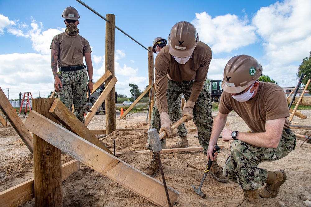 Seabees assigned to Naval Mobile Construction Battalion (NMCB) hammer in stakes to secure a log during an obstacle course construction project on aboard Naval Station Rota, Spain.