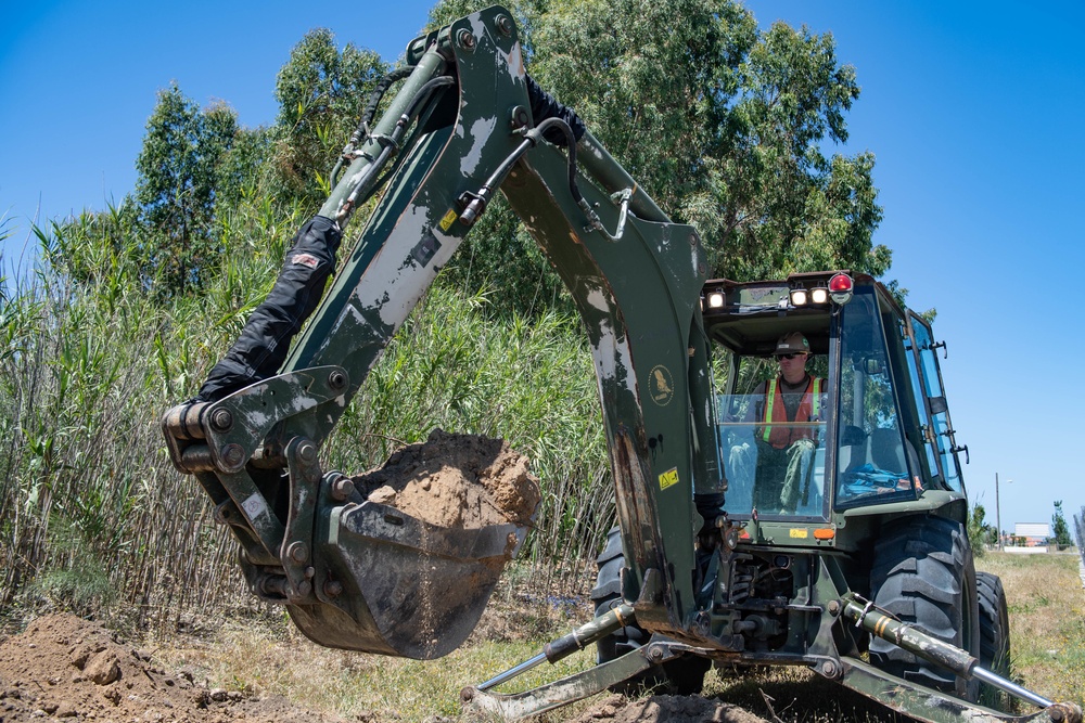 Seabees assigned to Naval Mobile Construction Battalion (NMCB) use a backhoe to excavate a trench during a street lighting construction project on aboard Naval Station Rota, Spain.