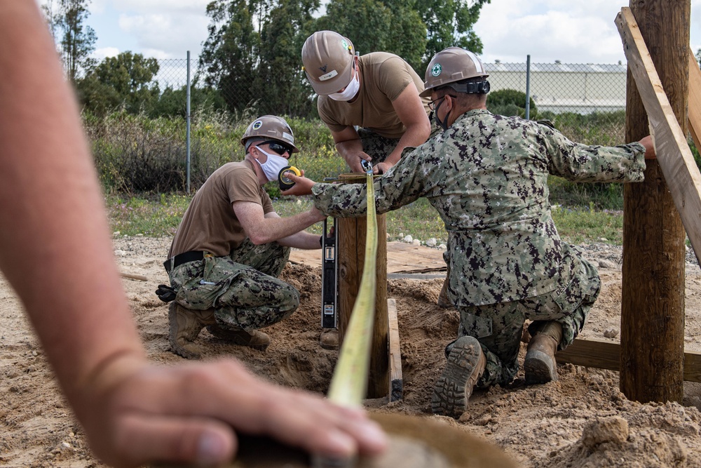 Seabees assigned to Naval Mobile Construction Battalion (NMCB) space and secure a log during an obstacle course construction project on aboard Naval Station Rota, Spain.