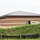 The image shows a large commercial or institutional building under construction, featuring concrete masonry unit (CMU) block walls with horizontal banding and a dark metal standing-seam roof. A white work truck is parked near an open door on the side of the building, suggesting active construction work. The foreground contains a grassy berm and a black silt fence, indicating active erosion control measures typical of a construction site.
