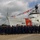 A large group of U.S. Coast Guard personnel pose for a formal crew photograph on a dock in front of Coast Guard Cutter 621. The vessel is dressed with international maritime signal flags strung from bow to stern, suggesting a ceremonial occasion. The ship displays the distinctive U.S. Coast Guard diagonal red stripe and emblem on its white hull.