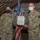 Two U.S. Air Force personnel in OCP (Operational Camouflage Pattern) uniforms are jointly holding a Department of the Air Force certificate, appearing to be an Air Force Achievement Medal presentation ceremony. Both individuals are wearing face masks, consistent with COVID-19 era protocols. A third masked service member stands in the background near an American flag.