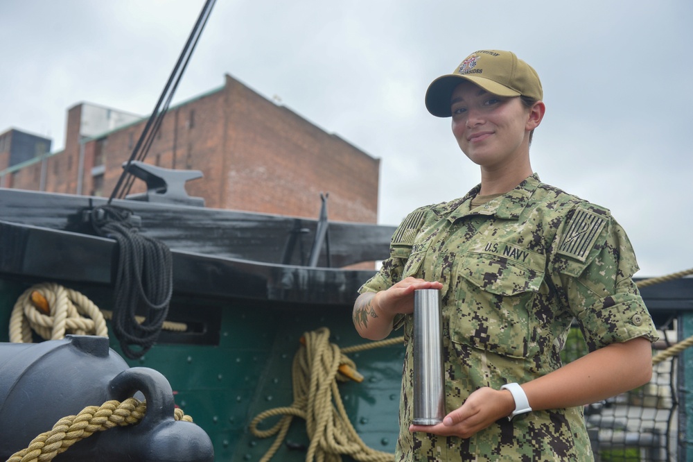 Airman Olivia Lawrence, assigned to USS Constitution, poses with a plugged and shined 40mm round from the saluting onboard Constitution