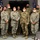 A group of approximately 11 military personnel pose together for a formal group photo in what appears to be an indoor facility. All individuals are wearing face masks, suggesting this photo was taken during the COVID-19 pandemic period. The group includes both male and female service members wearing various U.S. Air Force uniforms, with one individual in a flight suit.