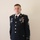 A male U.S. Army soldier is photographed in a formal portrait stance wearing the Army Service Uniform (ASU) in dress blue. His name tape reads 'TAYLOR' and he displays the rank insignia of a Staff Sergeant (E-6) on his sleeve. Multiple awards, badges, and ribbons are visible on his uniform chest.