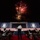 A military band performs outdoors at night beneath a fireworks display during what appears to be a formal U.S. presidential event. The stage backdrop prominently features two Presidential Seals on a red, white, and blue decorated platform. A conductor stands with his back to the camera, directing uniformed musicians seated in a semicircle on a red carpet.