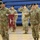 Korea's Top Dentist Changes Command A formal U.S. Army military ceremony taking place inside a gymnasium or indoor facility. Soldiers in OCP (Operational Camouflage Pattern) uniforms and black berets are rendering salutes, with one soldier holding a unit guidon. The guidon identifies the unit as the 618th DEN CO (Dental Company).