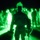 A night vision photograph showing a group of military personnel gathered outdoors in darkness. The image is captured through a night vision device, rendering everything in characteristic green monochrome tones. A central figure in the foreground is silhouetted against a bright green light source, with numerous other personnel visible in the background.