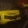 The image shows a close-up of a yellow K-90 Talisman XL breathing apparatus or gas detection device mounted on or near a firefighter's helmet. The equipment appears to be in active use in a smoky or low-light environment. A red helmet with a yellow tag is visible in the upper right portion of the frame.