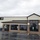 The image shows a commercial building identified as a 'Commissary' with the address number 1537 visible near the entrance. The building features brick and stucco construction with a dark metal roof, large tinted windows, and a wet parking lot indicating recent rainfall. The lot includes marked handicap-accessible parking spaces and appears largely empty.