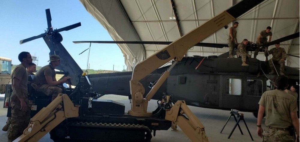 Soldiers conduct maintenance on a UH-60 Black Hawk helicopter using a self-propelled crane aircraft maintenance and positioning II expeditionary crane.  The SCAMP II is used to move major pieces of the helicopter.
