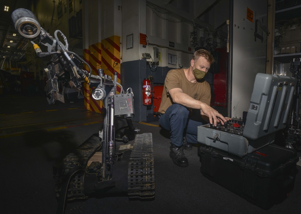 Sailor Troubleshoots Talon Explosive Ordnance Disposal (EOD) Robot In Hangar Bay Aboard Aircraft Carrier USS Nimitz CVN 68