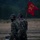 Two U.S. Army soldiers in MultiCam (OCP) camouflage uniforms are walking in heavy rain, one carrying a red unit guidon flag. The flag displays the number '112,' the letter 'C,' and crossed cannon insignia indicating a Field Artillery unit. Both soldiers are wearing face coverings and bear a shoulder patch consistent with the 4th Infantry Division.
