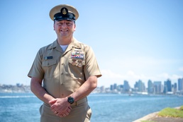 Senior Chief Cryptologic Technician (Collection) Jamey Stewart poses for a photo in front of the San Diego skyline