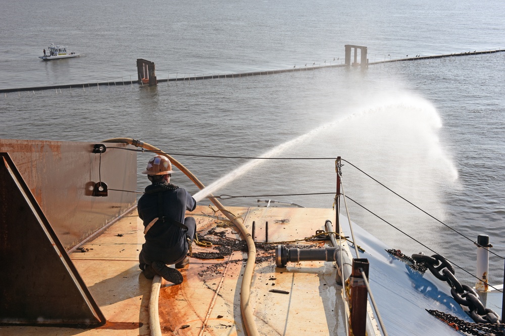 A responder aims a fire hose on top of the Golden Ray wreck during a fire drill