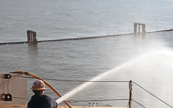 A responder aims a fire hose on top of the Golden Ray wreck during a fire drill