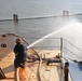 A responder aims a fire hose on top of the Golden Ray wreck during a fire drill